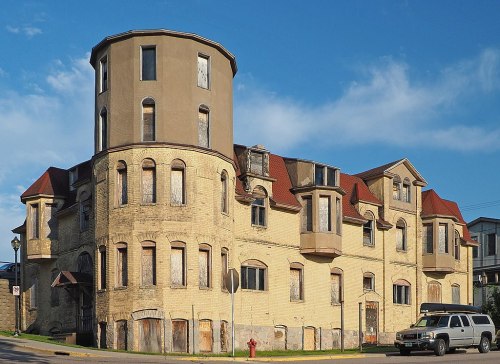 Abandoned building with a unique architectural design, featuring a round tower and boarded windows against a blue sky.