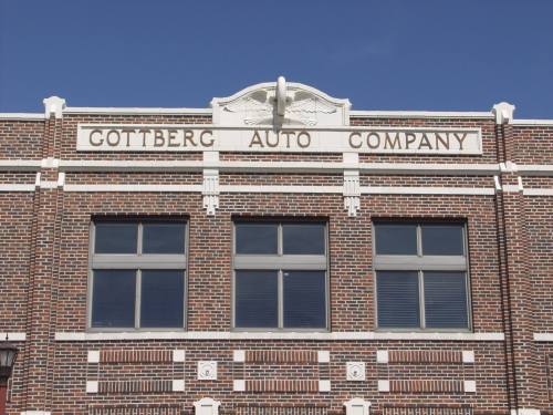 Brick building facade with the sign "Cottberg Auto Company" above large windows against a clear blue sky.