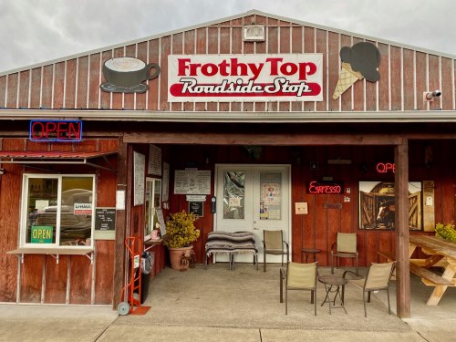 Exterior of Frothy Top Roadside Stop, featuring a wooden facade, open sign, and outdoor seating area.