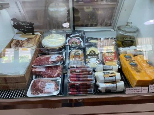 Display case filled with various meats, cheeses, and baked goods, including bacon, steaks, and desserts.