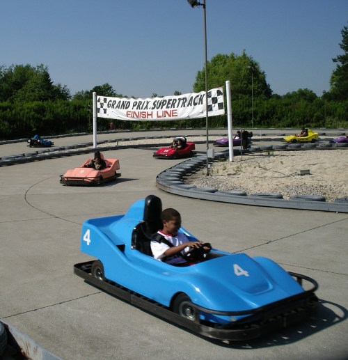 A go-kart track with several colorful karts racing towards the finish line under a checkered banner.