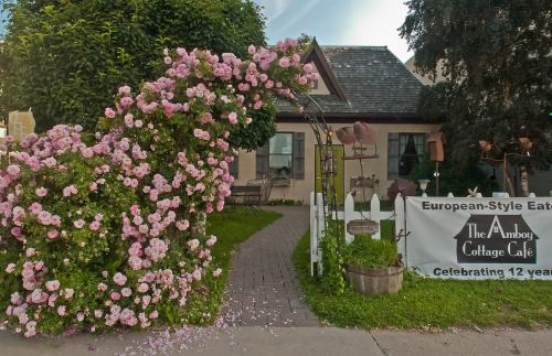 A charming café with a flower-covered archway, outdoor seating, and a sign celebrating 12 years in business.