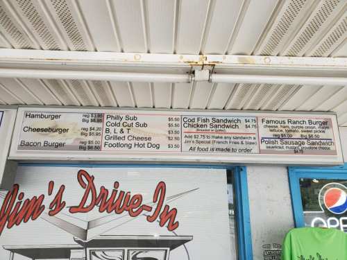 Menu board at a drive-in featuring burgers, sandwiches, and hot dogs with prices listed. All food is made to order.