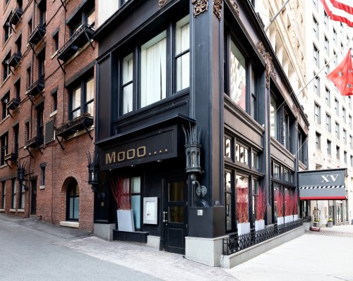 Exterior view of a stylish restaurant named "MOOO..." with large windows and decorative elements, located on a city street.