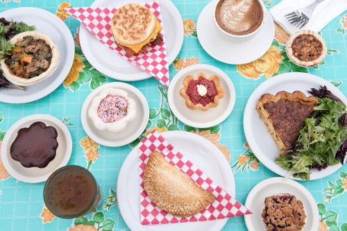 A colorful table spread with various dishes, including sandwiches, desserts, and salads on a patterned tablecloth.