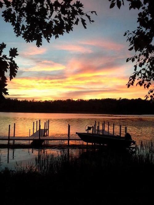 A serene lake at sunset, with colorful skies and silhouettes of boats and trees along the water's edge.