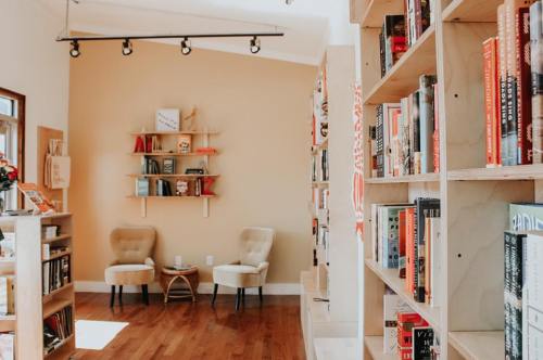 Cozy reading nook with two chairs, a small table, and bookshelves filled with books against a warm-toned wall.