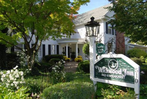 A charming bed and breakfast with a white exterior, surrounded by greenery and flowers, featuring a welcoming sign.
