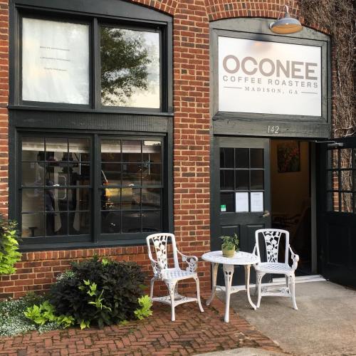 Exterior of Oconee Coffee Roasters in Madison, GA, featuring brick walls, large windows, and outdoor seating.