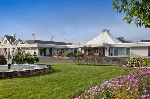 A welcoming hotel entrance with a fountain, colorful flowers, and a clear blue sky in the background.