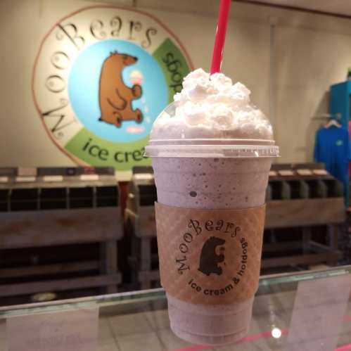 A frosty milkshake topped with whipped cream, displayed in front of a colorful ice cream shop sign.