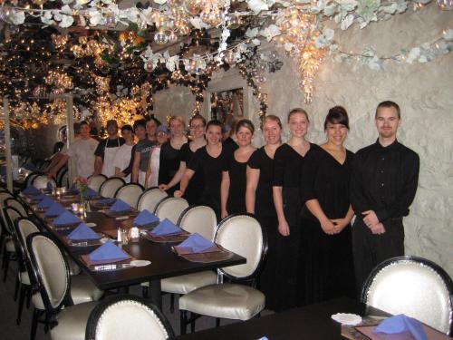 A group of servers in black attire stands in a decorated restaurant with a long table set for dining.
