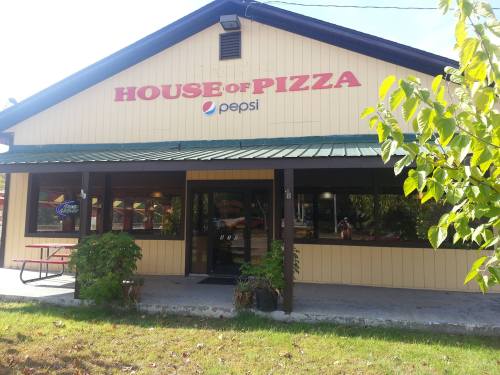 Exterior of a restaurant named "House of Pizza," featuring a Pepsi sign and a green roof, surrounded by grass and trees.