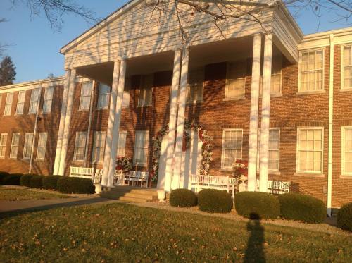 A brick building with white columns, decorated with wreaths, surrounded by manicured bushes and a grassy lawn.