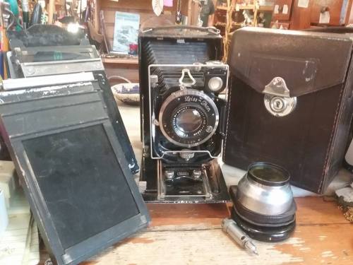 An antique camera with a large lens, surrounded by film holders and a leather case on a wooden surface.