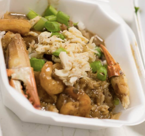 A takeout container filled with shrimp, crab, rice, and green onions.