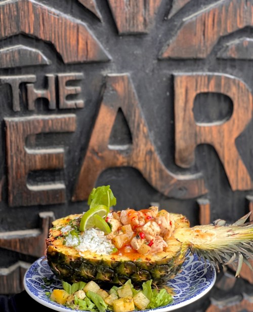 A pineapple bowl filled with rice, chicken, and garnished with lime, served with a side of salad.