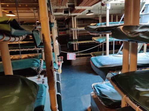 Interior view of a ship's bunk area with stacked sleeping quarters and a sign hanging in the middle.