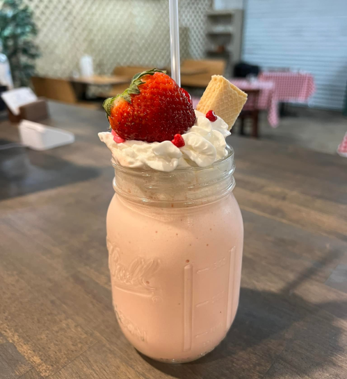 A creamy pink milkshake topped with whipped cream, a strawberry, and a wafer, served in a mason jar.