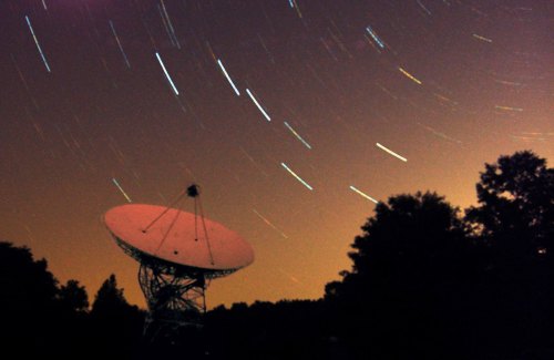 A satellite dish under a starry sky, with star trails creating a dynamic effect around it.