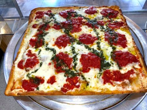 A square pizza topped with red sauce, dollops of pesto, and melted cheese on a golden crust.