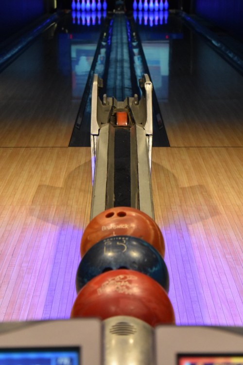 A view down a bowling lane with colorful bowling balls stacked on a rack in the foreground.