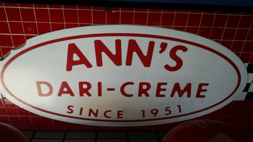 Sign for Ann's Dari-Creme, featuring red text on a white background, with a red tiled wall in the background.