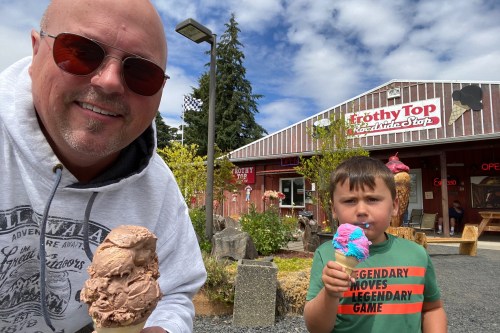 A man and a boy enjoy colorful ice cream cones outside a shop called Frothy Top on a sunny day.