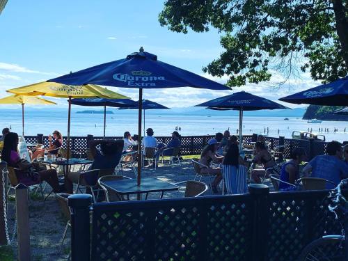 A beachside café with umbrellas, people enjoying drinks, and a view of the ocean and distant mountains.