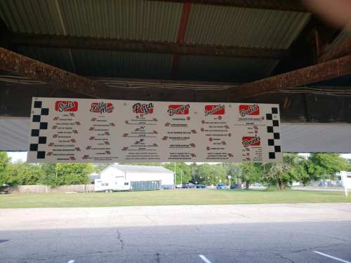 Menu board displaying various food options like pizza, burgers, and sides, hanging under a covered area.