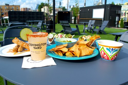 A table with a colorful spread of tacos, chips, salsa, and a drink in a vibrant outdoor setting.