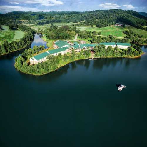 Aerial view of a lush green landscape with a lake and a resort building surrounded by trees and hills.