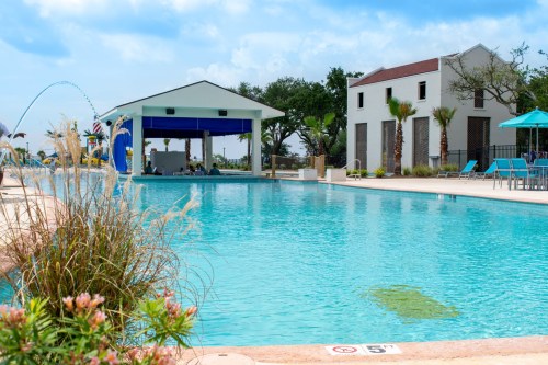 A serene pool area with a blue canopy, palm trees, and lounge chairs under a clear sky.