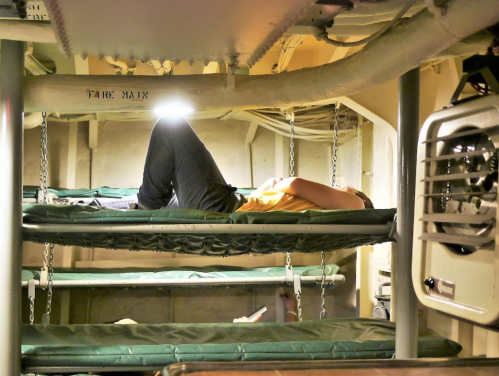 A person lies on a bunk bed in a dimly lit space, with a light shining above them.