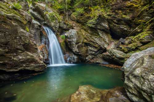 A serene waterfall cascades into a clear pool, surrounded by rocky cliffs and lush greenery.