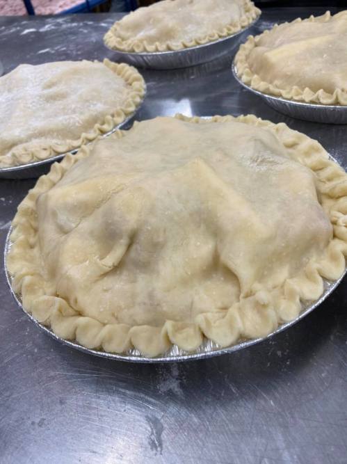 Four unbaked pies with crimped edges, covered with a smooth layer of dough, resting on a metal surface.