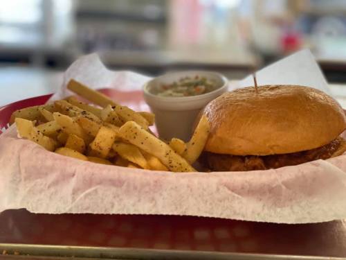 A plate with a sandwich, fries, and a small cup of coleslaw, served in a red basket with white paper.