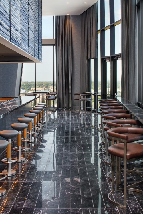 Modern bar interior with high stools, sleek black flooring, large windows, and elegant curtains.