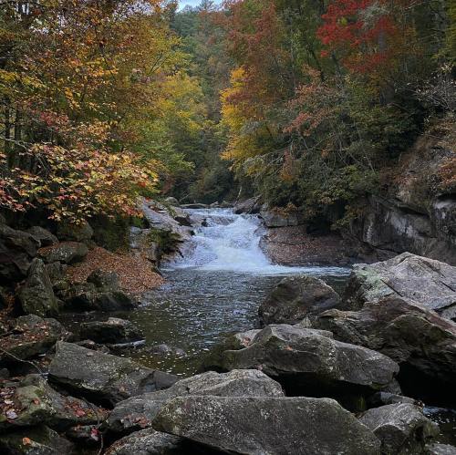 A serene river flows through a rocky landscape, surrounded by vibrant autumn foliage in warm colors.