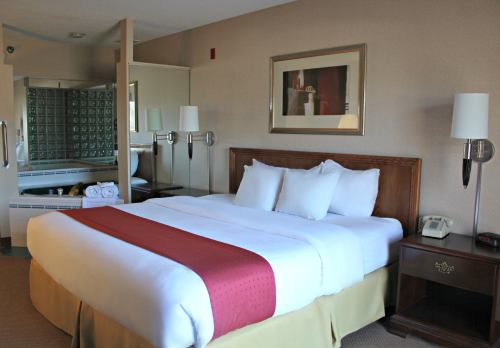 A cozy hotel room featuring a king-sized bed, bedside lamps, and a bathroom with a glass block wall in the background.