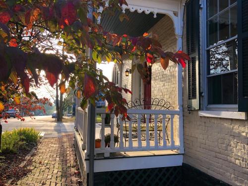 A cozy porch with a white railing, surrounded by autumn leaves and sunlight, inviting a warm atmosphere.