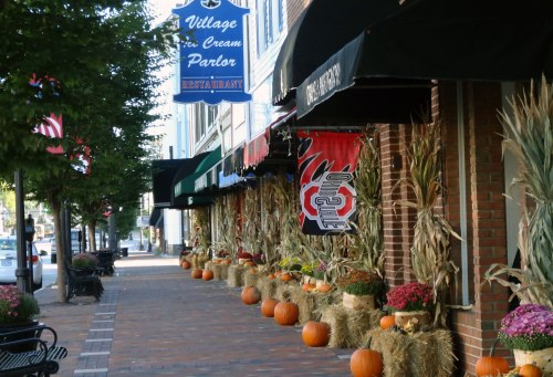 A charming street lined with shops, decorated with pumpkins, hay bales, and autumn flowers for the fall season.