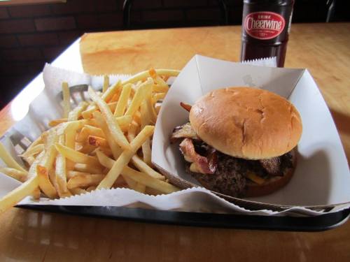 A burger with bacon and cheese served with a side of golden fries and a bottle of Cheerwine soda.