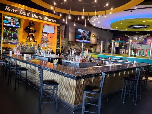 A vibrant bar area with a black countertop, colorful decor, and multiple TVs displaying sports news.