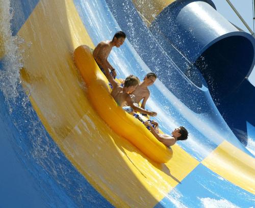 Four people in a yellow inflatable raft slide down a colorful water slide, splashing water around them.