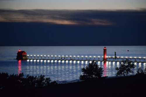 A pier with red lighthouses illuminated at night, reflecting on calm water under a dark sky.