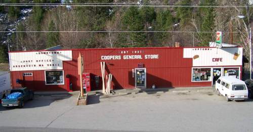 A red general store and café in a small town, surrounded by trees and mountains, with signs for downtown and uptown.