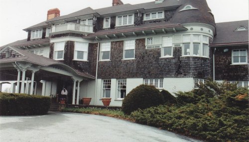 Historic building with a shingled exterior, large windows, and a welcoming entrance surrounded by manicured landscaping.