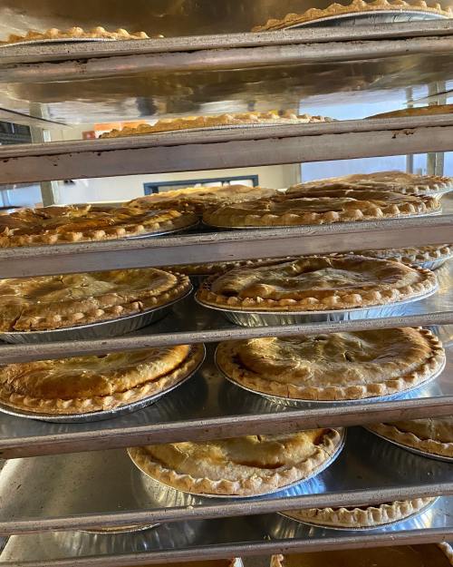 A stack of freshly baked pies cooling on metal racks in a bakery.