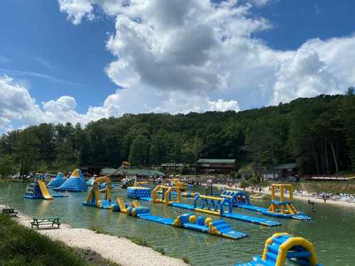 A vibrant water park with inflatable structures on a lake, surrounded by trees and a clear blue sky.